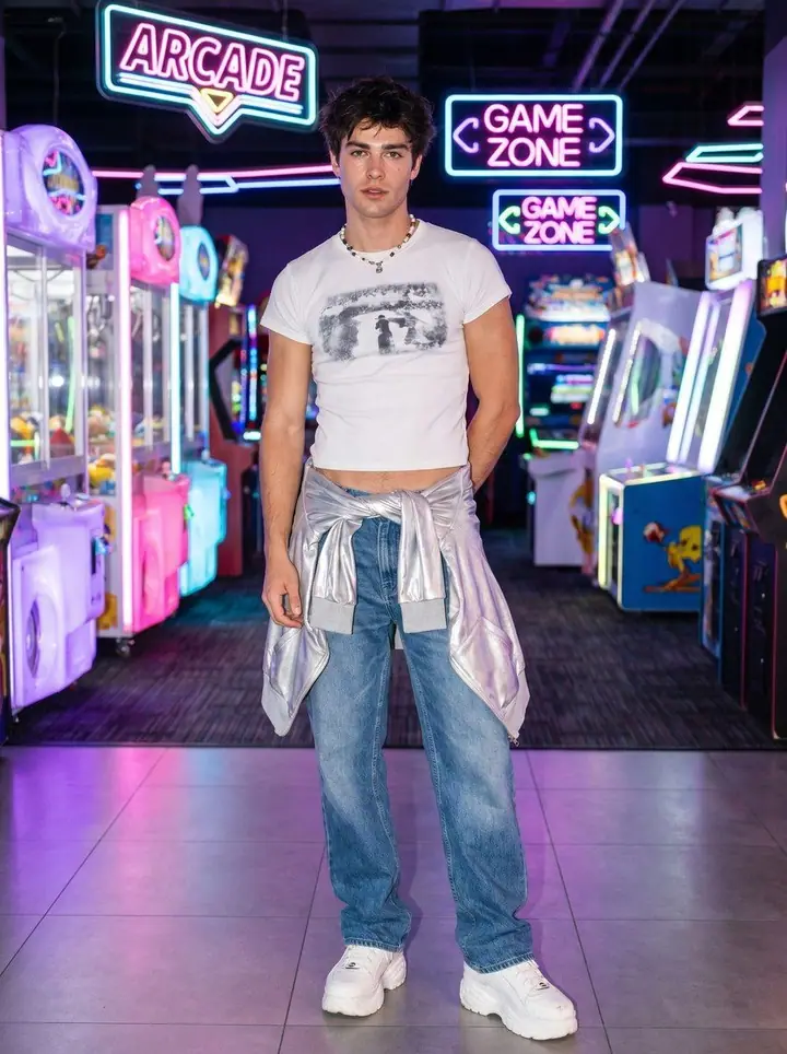 Y2K, menswear: a cropped photo-print tee, baggy jeans and a silver jacket tied at the waist in a neon arcade.